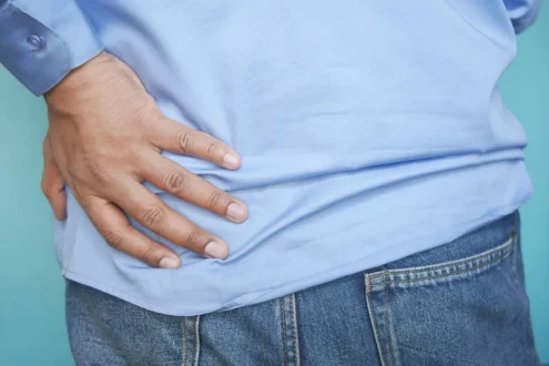 شخص يمسك ظهره بألم مع خلفية طبية توحي بالبحث عن أسباب ألم الظهر والسرطان