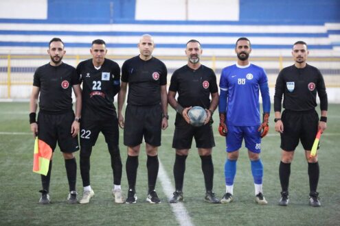 لقطة من مباراة في دوري الدرجة الأولى الأردني تظهر لاعبين يتنافسون على الكرة، مع شعار الدوري في الخلفية.