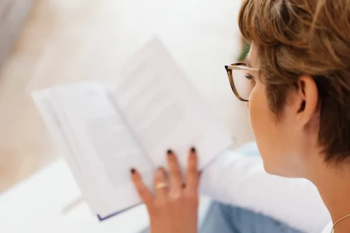 امرأة في الأربعينات ترتدي نظارات قراءة وتنظر إلى كتاب